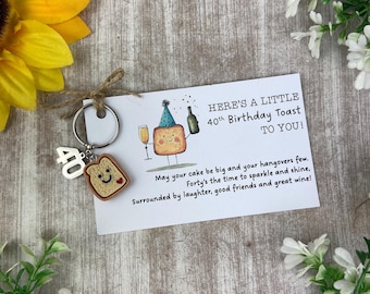 May include: A 40th birthday-themed keychain with a wooden toast charm and a card. The card reads "Here's a little 40th Birthday Toast to You!" with a cartoon cake illustration. The keychain also has a "40" charm.