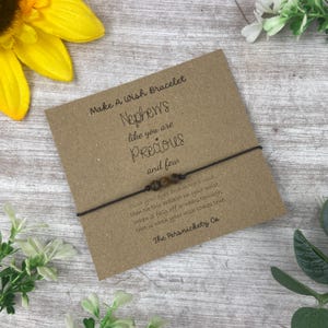 May include: A brown wish bracelet with brown beads and a card that reads "Make A Wish Bracelet Nephews like you are Precious and few" and "close your eyes and make a wish then tie this bracelet on your wrist, when it falls off or wears through, that is when your wish comes true. The Persnickety Co"