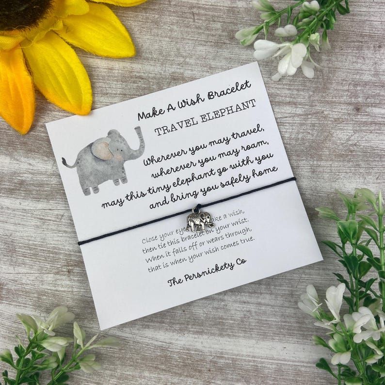 May include: A black string bracelet with a silver elephant charm. The card attached to the bracelet reads "Make A Wish Bracelet Travel Elephant" and includes a poem about the elephant bringing you safely home.