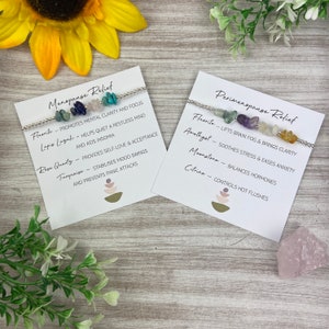 May include: Two white cards with black text describing the benefits of crystals for menopause and perimenopause relief. Each card features a silver bracelet with different colored crystals.