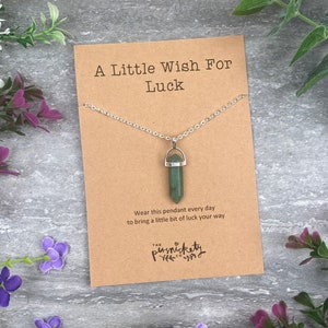 May include: A silver chain necklace with a green crystal pendant. The card reads "A Little Wish For Luck" and "Wear this pendant every day to bring a little bit of luck your way." The card also has the text "The Persnickety Co."