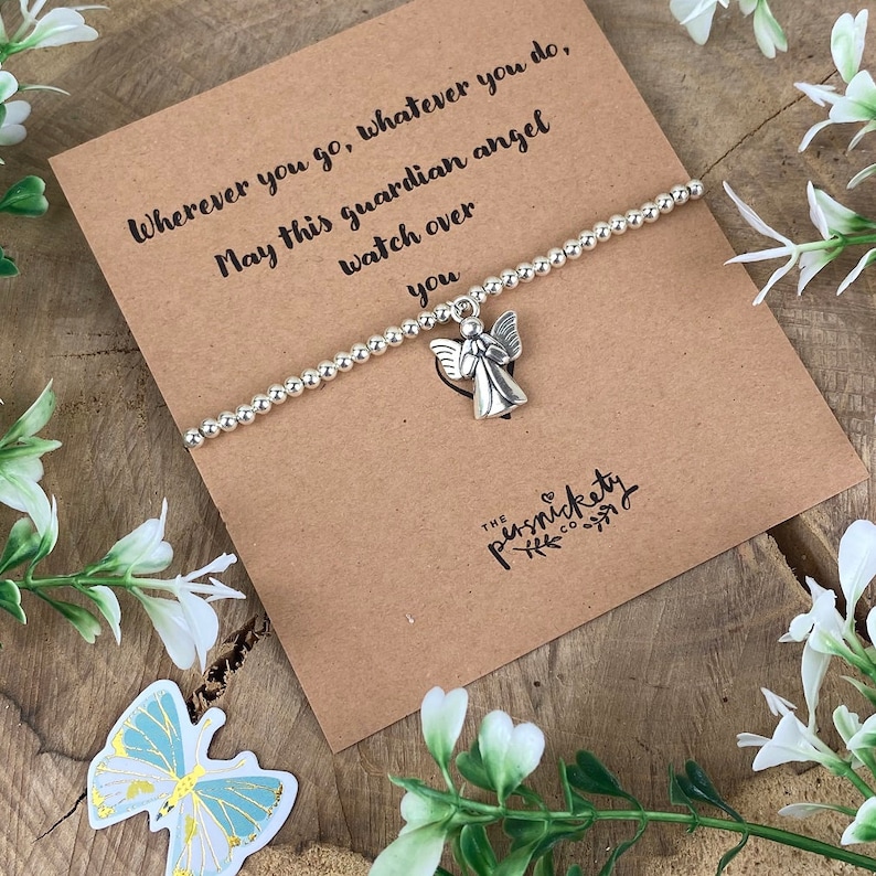 May include: A silver bracelet with a small angel charm. The bracelet is on a brown card with the text "Wherever you go, whatever you do, May this guardian angel watch over you" and the logo "THE pernickety CO."