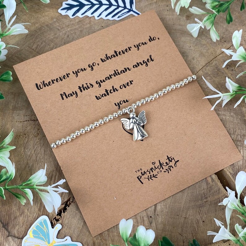 May include: A silver charm bracelet with an angel charm. The bracelet is on a brown card with the text "Wherever you go, whatever you do, May this guardian angel watch over you" and "THE PERNICKETY CO."