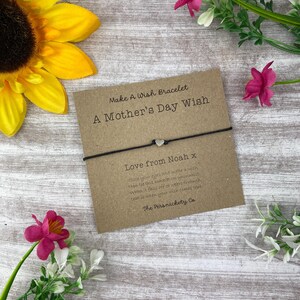 May include: A brown card with the text "Make A Wish Bracelet A Mother's Day Wish" and "Love from Noah x" with a black string bracelet with a silver heart charm.