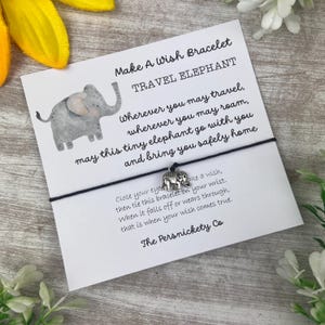 May include: A black string bracelet with a silver elephant charm. The card attached to the bracelet reads "Make A Wish Bracelet Travel Elephant" and includes a message about making a wish when the bracelet falls off.