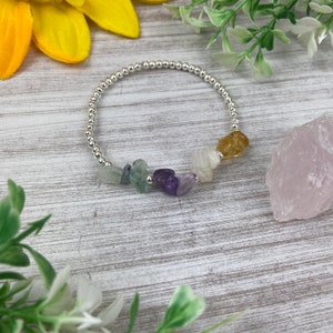 May include: A silver beaded bracelet with a variety of colorful gemstones, including green, purple, white, and yellow.
