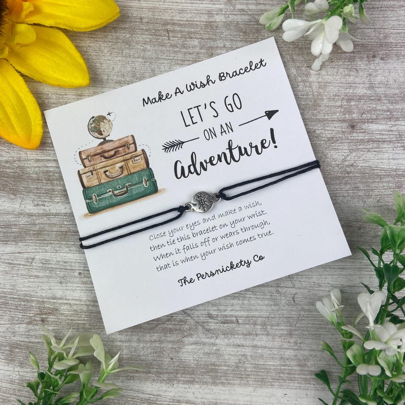 May include: A black wish bracelet with a silver charm is displayed on a white card. The card reads "Make A Wish Bracelet" and "LET'S GO ON AN Adventure!" with an illustration of stacked suitcases. Text on the card explains how to use the bracelet.