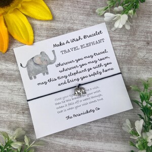 May include: A white card with a gray elephant illustration and black text that reads "Make A Wish Bracelet Travel Elephant" and "Wherever you may travel, wherever you may roam, may this tiny elephant go with you and bring you safely home".  The card is attached to a black string with a silver elephant charm.
