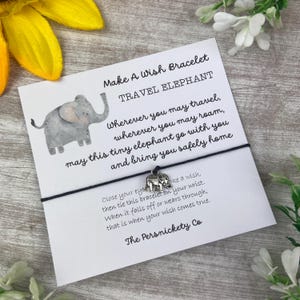 May include: A black string bracelet with a silver elephant charm. The card attached reads "Make A Wish Bracelet Travel Elephant" and includes a message about the elephant bringing you safely home. Close your eyes, make a wish, and tie the bracelet on your wrist. When it falls off or wears through, your wish will come true. The card is signed "The Persnickety Co."