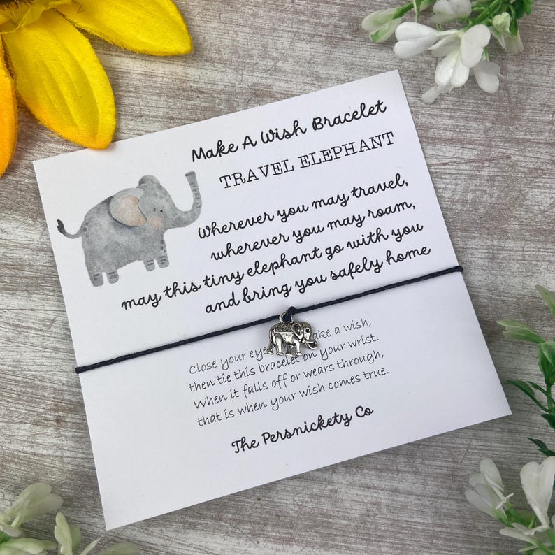 May include: A black string bracelet with a silver elephant charm. The card attached reads "Make A Wish Bracelet Travel Elephant" and includes a message about the elephant bringing you safely home. Close your eyes, make a wish, and tie the bracelet on your wrist. When it falls off or wears through, your wish will come true. The card is signed "The Persnickety Co."