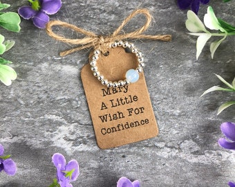 May include: A silver beaded ring with a light blue gemstone, on a brown tag with the text "Mary A Little Wish For Confidence".