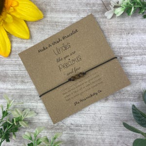 Könnte beinhalten: Eine braune Karte mit dem Text "Make A Wish Bracelet" und "Uncles like you are Precious and few". Ein braunes Armband aus Schnur mit braunen Perlen ist an der Karte befestigt.