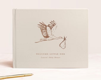 May include: A white guest book with a brown stork illustration carrying a baby bundle. The text on the cover reads "Welcome Little One" and "Lauren's Baby Shower".