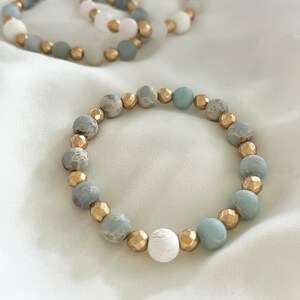 May include: A bracelet made of light blue and gold beads. The bracelet has a white bead in the center.