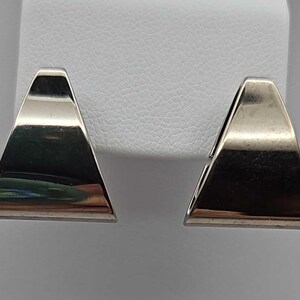 May include: A pair of silver-toned, triangular earrings. Each earring has a flat, polished surface and a geometric shape. The earrings are displayed against a white background, highlighting their reflective quality and minimalist design.