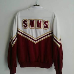 May include: White and maroon varsity jacket with the letters "SVHS" embroidered on the back in gold. The jacket has a zipper closure and long sleeves.
