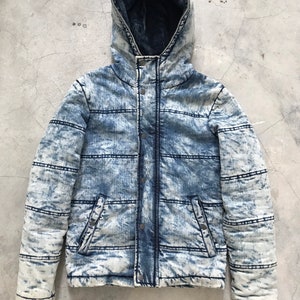 Puede incluir: Una chaqueta vaquera azul claro con capucha. La chaqueta tiene un diseño acolchado y una cremallera.