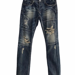 Op de afbeelding: Gedragen blauwe denim jeans met meerdere patches en scheuren. De jeans hebben een rechte pijp en een klassieke vijf-zak stijl.