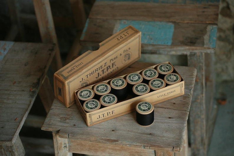 Puede incluir: Una caja de carretes de hilo negro con la etiqueta "J. Thiriez Pere & Fils J.T.P.F. Lille Paris" en la caja.