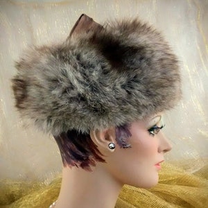 May include: A brown fur hat with a brown leather band. The hat is worn by a mannequin with a pearl necklace.