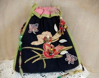 May include: A black fabric drawstring bag with a green trim and a floral design. The bag has a beaded strap with a charm that says "Mary Frances".