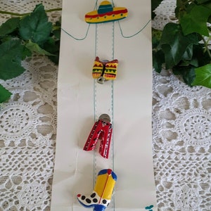 May include: A set of four colorful ceramic buttons featuring a sombrero, a saddle, a pair of red pants, and a cowboy boot. The buttons are displayed on a white card with the word "Serci" printed on the bottom.