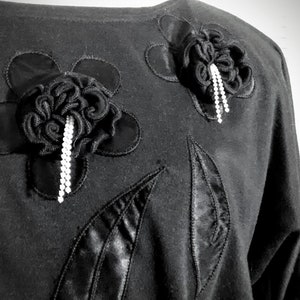 May include: Black shirt with two large black fabric flowers with rhinestone embellishments.