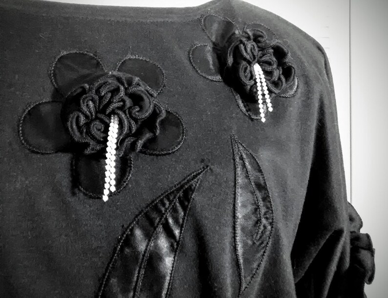 May include: Black shirt with two large black fabric flowers with rhinestone embellishments.