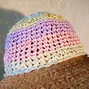 Puede incluir: Un sombrero de paja de ala ancha con una corona de ganchillo en tonos de rosa, morado y amarillo.