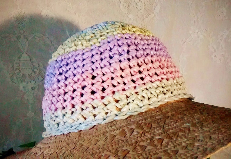 Puede incluir: Un sombrero de paja de ala ancha con una corona de ganchillo en tonos de rosa, morado y amarillo.