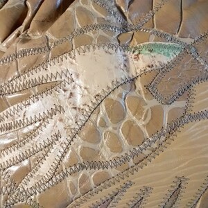 May include: Close-up of a beige leather purse with a crocodile-embossed pattern. The purse is made of several pieces of leather sewn together with a zig-zag stitch.