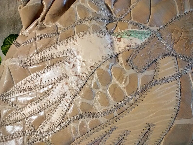 May include: Close-up of a beige leather purse with a crocodile-embossed pattern. The purse is made of several pieces of leather sewn together with a zig-zag stitch.