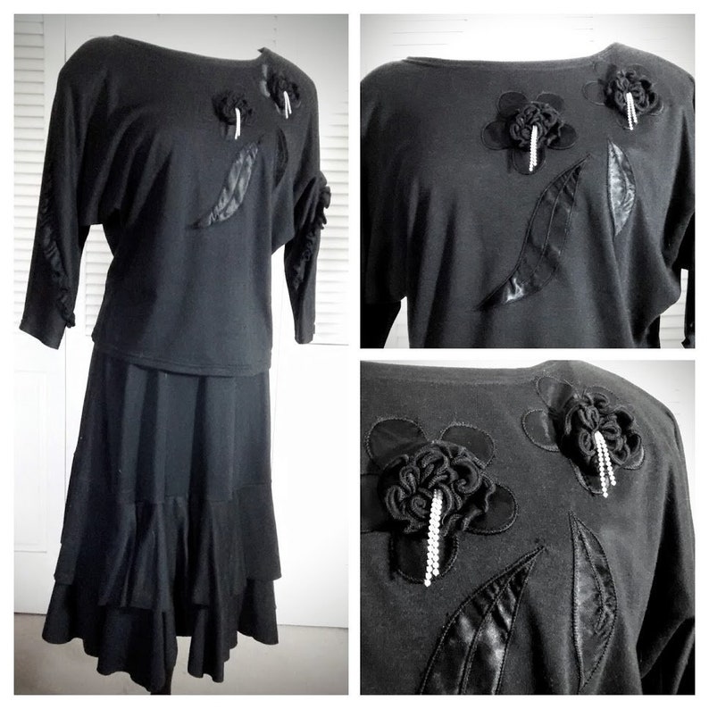 May include: A black two-piece outfit with a ruffled skirt and a top featuring black fabric flowers with rhinestone accents.