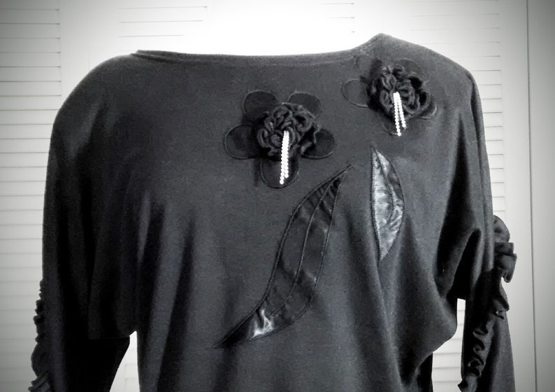 May include: Black long-sleeved shirt with a scoop neck and decorative black fabric flowers and leaves.