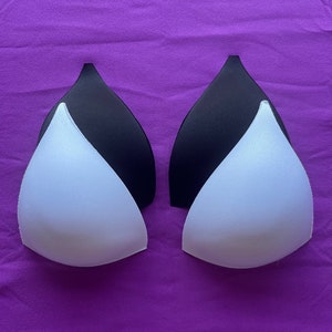 Puede incluir: Dos pares de insertos de sujetador, uno blanco y uno negro, sobre un fondo morado.