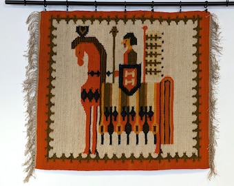 May include: A woven wall tapestry featuring a knight on horseback. The tapestry is made of wool and has a fringe border. The colors are orange, brown, green, and white.