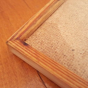 May include: Close-up of a rectangular wooden picture frame with a light brown finish. The frame has a natural wood grain and a simple, classic design. The backing is a light brown, textured material.
