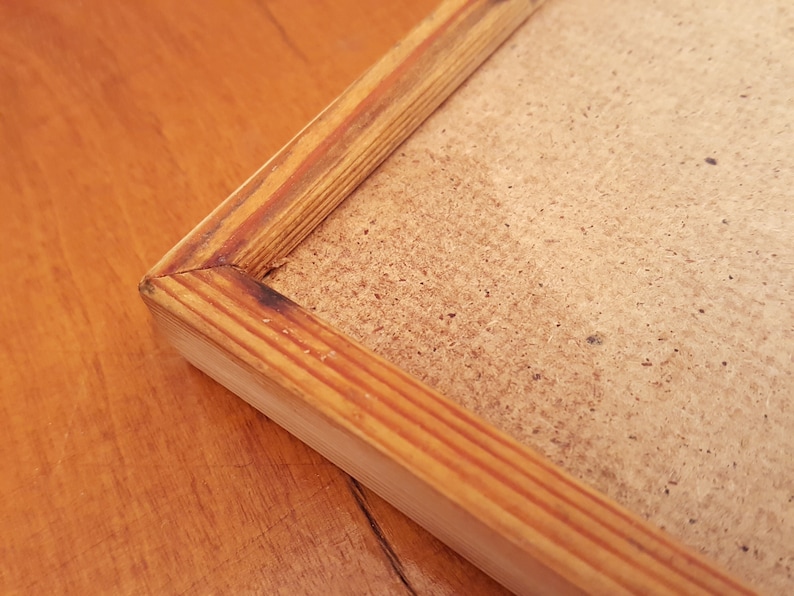 May include: Close-up of a rectangular wooden picture frame with a light brown finish. The frame has a natural wood grain and a simple, classic design. The backing is a light brown, textured material.