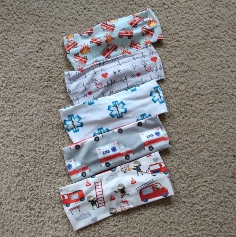 May include: Five different patterned headbands. The headbands are made of a soft, stretchy fabric. The patterns include fire trucks, hearts, stars, and ambulances.