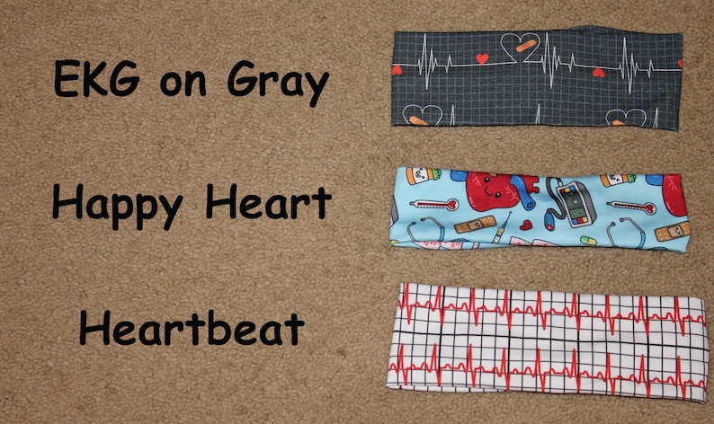 May include: Three headbands with different medical-themed prints. The top headband has a black and white EKG pattern with red hearts. The middle headband has a light blue background with a red heart, a stethoscope, a thermometer, and other medical symbols. The bottom headband has a white background with a red EKG pattern.