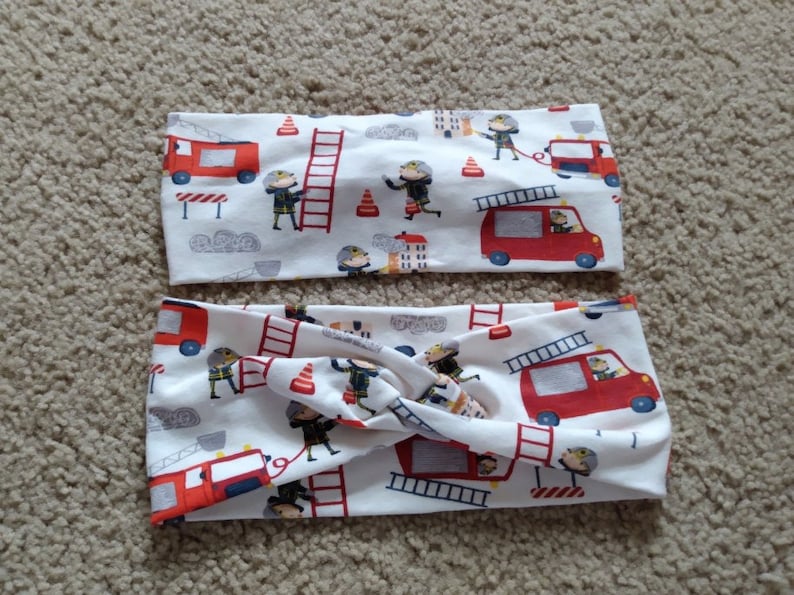 May include: Two white fabric headbands with a red, white, and blue fire truck and firefighter pattern.