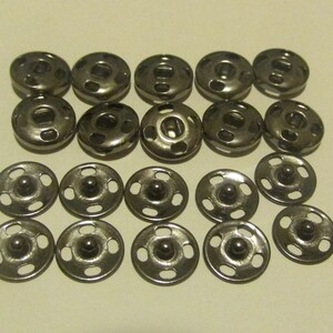 May include: A set of 18 silver metal snap fasteners. The fasteners are round and have a raised center. They are arranged in two rows of nine.