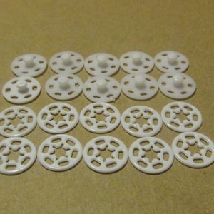 May include: A collection of white plastic snaps, some with a centre post and others with a star-shaped cutout.