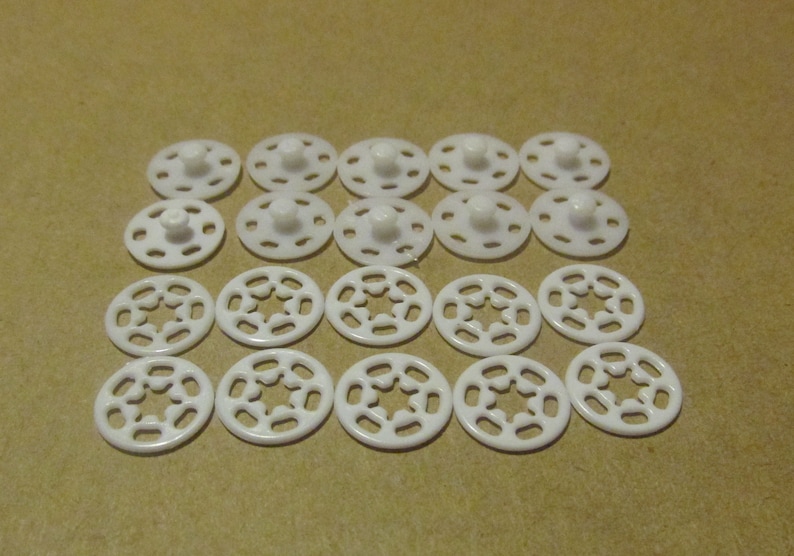 May include: A collection of white plastic snaps, some with a centre post and others with a star-shaped cutout.
