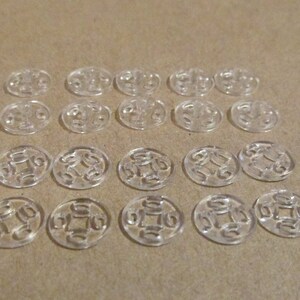 May include: Twenty-four clear plastic buttons with a decorative design. The buttons are arranged in four rows of six buttons each.