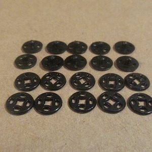 May include: A set of 18 black plastic snap buttons with a decorative design. The buttons are arranged in three rows of six.