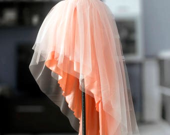 Puede incluir: Una falda de tul de color melocotón con un dobladillo alto-bajo. La falda está en un maniquí y tiene una cintura de satén. El texto "By Aysya Kolarova MADE TO MEASURE" está en la parte superior de la imagen.