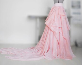May include: A light pink tulle skirt with multiple layers and a long train. The skirt is on a dress form.