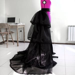 May include: A black tulle skirt with multiple layers and a ruffled design. The skirt is worn on a pink dress form.
