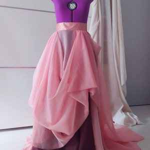 May include: A pink and burgundy layered tulle skirt with a satin waistband. The skirt is on a dress form and has a flowing, voluminous shape.